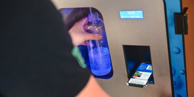 Člověk si čepuje vodu do lahve s pomocí aplikace