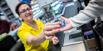 Pokladní supermarketu přebírá Bertík žeton od zákazníka 