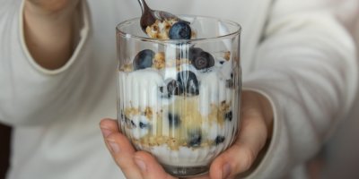 Žena drží sklenici s jogurtem, ovesnými vločkami a borůvkami