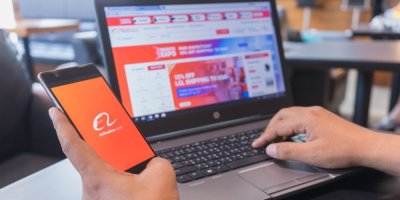 Muž drží v ruce mobilní telefon s aplikací Alibaba, má u toho otevřený notebook