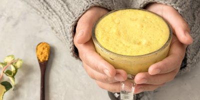 Ruce ve svetru držící šálek zlatého mléka