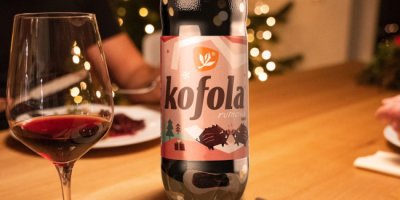 Lahev Kofoly a sklenice s červeným vínem na stole