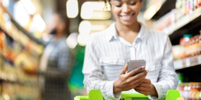 Žena se dívá do mobilu v supermarketu
