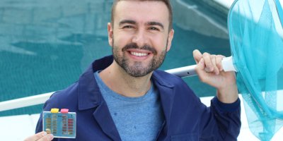 Usmívající se muž u bazénu se síťkou a měřidlem ph