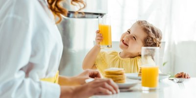 Holčička pije pomerančový džus a usmívá se u toho na maminku