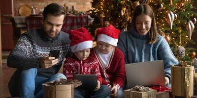 Rodina u vánočního stromečku kouká do mobilů, tabletů a notebooku