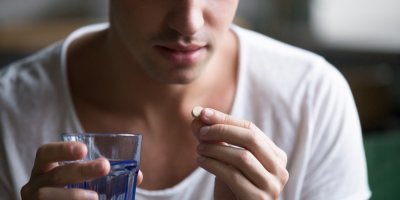 Muž v jedné ruce drží pilulku, v druhé sklenici s vodou