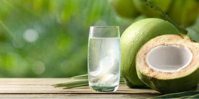 Kokosová voda ve sklenici, v pozadí dva kokosy