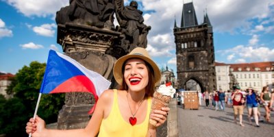 Žena na Karlově mostě drží v jedné ruce trdelník se šlehačkou a v druhé českou vlajku