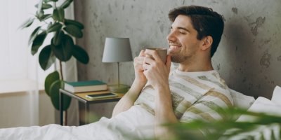 Muž v posteli pije nápoj z hrnku a usmívá se