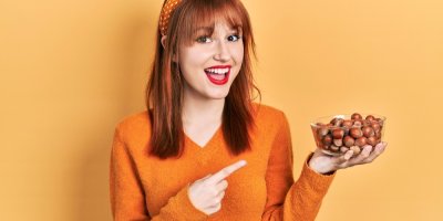 Žena ve svetru ukazuje na misku s oříšky