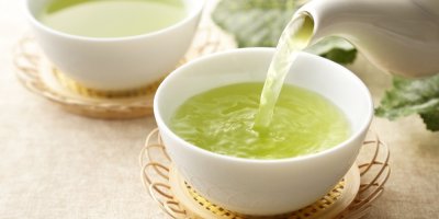 Dva šálky se zeleným čajem, do jednoho se nalévá čaj z konvice