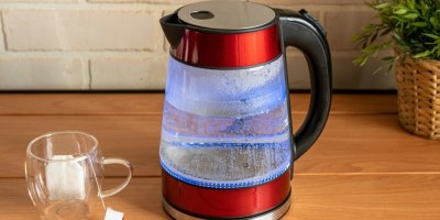 Rychlovarná konvice s vodou, položená na stole, vedle prázdný šálek na čaj