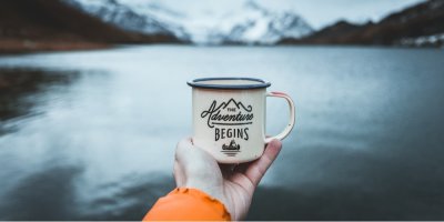 Hrnek, položený na dlani, v pozadí jezero a hory