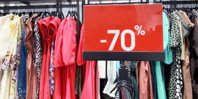 Regál s oblečením, na kterém je umístěna cedule upozorňující na slevu