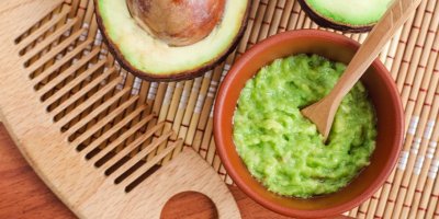 Miska s rozmačkaným avokádem, vedle je položený hřeben a rozpůlené avokádo