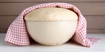 Vykynuté těsto ve skleněné míse, přikryté utěrkou