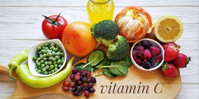 Na dřevěném prkénku jsou brokolice, jahody, pomeranč, citron, rajče, špenát, nápis vitamin C