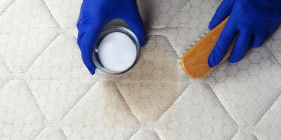 Ruce v rukavicích čistí špinavou matraci