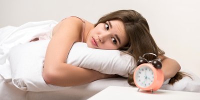 Žena kouká smutně z postele na budík