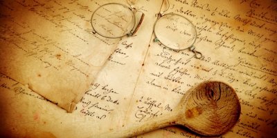 Stará, ručně psaná kuchařka, na které je položená vařečka