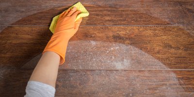 Ruka v rukavici umývá hadrem zaprášený stůl