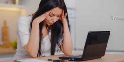 Žena má hlavu v dlaních a před ní leží notebook