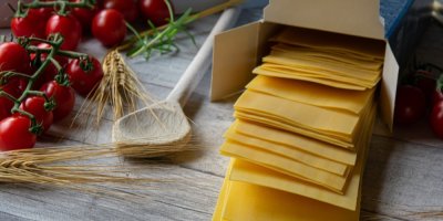 Rozbalené balení lasagní, vedle poležená cherry rajčata a vařečka