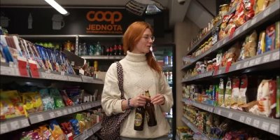 Žena, nakupující v COOPu, s pivem v ruce