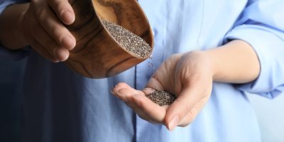 Žena sype chia semínka z dřevěné misky do dlaně