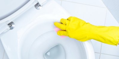 Ruka ve žluté rukavici čistí záchod