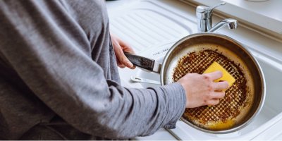 Člověk čistí připálenou pánev houbičkou