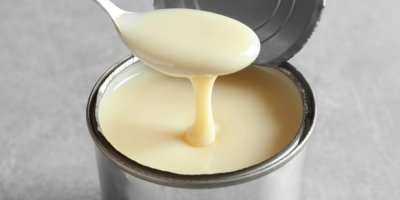 Otevřená plechovka s kondenzovaným mlékem a lžíce, která z ní nabírá mléko