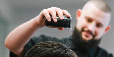 Muž aplikuje jinému muži pudr na vlasy