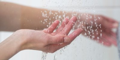 Žena zkouší rukou teplotu vody ze sprchy