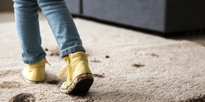 Dítě v zablácených teniskách šlape po koberci