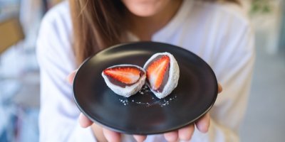 Člověk drží talířek, na kterém jsou mochi s čokoládou a malinami