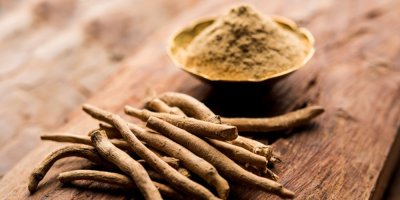 Kořen ašvagandy na stole, vedle ní je miska s práškem z ašvagandy