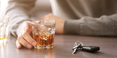 Muž drží sklenku s alkoholem a vedle jsou položené klíče od auta