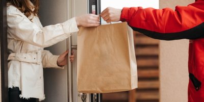 Kurýr předává ženě papírovou tašku s jídlem