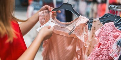 Žena drží v obchodě šaty a dívá se na lístek