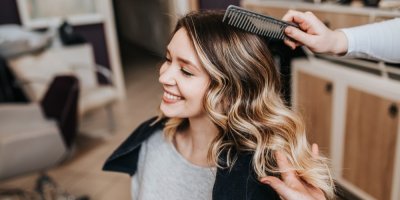 Žena s vlnitými vlasy se směje a někdo ji češe