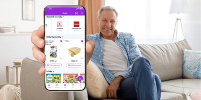 Muž sedí na gauči a ukazuje displej mobilního telefonu s aplikací Kupi