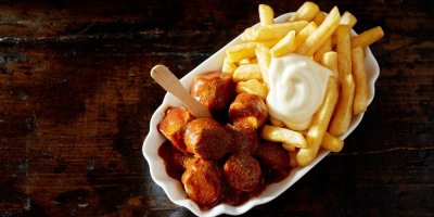 Currywurst s hranolkami a tatarkou, servírovaný v bílé keramické misce