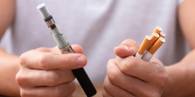 Ruce, které drží elektronickou cigaretu a v druhé klasické cigarety