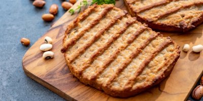 Rostlinné opečené maso na dřevěném prkénku, okolo jsou fazole