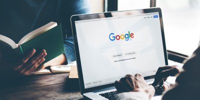 Osoba má na notebooku otevřený google, další si čte knihu