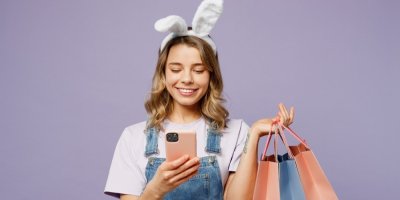 Dívka se zaječími oušky drží v ruce tašky a dívá se do mobilu