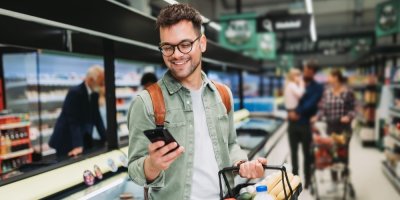 Muž v brýlích nakupuje a dívá se zároveň do mobilu