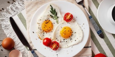 2 sázená vejce, servírovaná na bílém talíři s cherry rajčátky